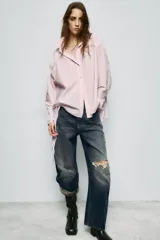 Camisa de corte oversize con cuello solapa y escote en pico. Presenta manga larga con puños abotonados, cierre frontal con botones y detalle de lazada ajustable en la espalda.