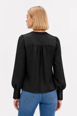 Camisa negra de poliéster satinado, de corte holgado, con cuello en V, cierre frontal abotonado y mangas largas con puños estructurados.