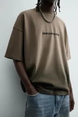 Camiseta de corte relajado (relaxed fit) con cuello redondo y manga corta. Presenta un estampado frontal con relieve en la zona del pecho con el texto "Endless Echo", y un efecto de teñido degradado que va del marrón claro al marrón oscuro/negro en la parte inferior.