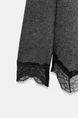 Top de manga larga en tejido suave color gris, con cuello redondo y bajo asimétrico decorado con encaje negro a tono. Presenta detalles de encaje negro en los puños.