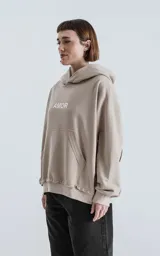 Buzo con capucha color beige claro, de calce oversize crop, con costuras expuestas en mangas y ruedo deshilachado. Presenta la palabra "AMOR" estampada en el pecho en color blanco.