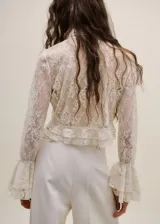 Blusa de encaje color crema con cuello alto, mangas largas con volados en los puños y detalle de volado en el ruedo.