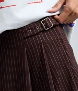 Short pollera de estilo sastre con patrón de rayas finas, diseño estructurado con pliegues delanteros y hebilla lateral ajustable.