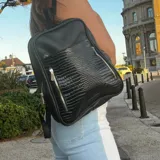 Mochila negra de cuero con textura simil cocodrilo en el bolsillo frontal.