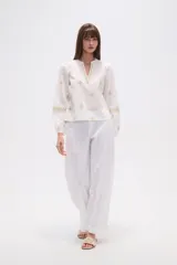 Blusa de algodón color tostado con cuello mao y escote en V. Presenta mangas largas abullonadas con puños elásticos y un diseño con bordados geométricos en contraste distribuidos por toda la prenda.