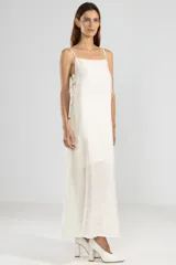 Vestido largo color crema de lyocell, poliamida y lino, con breteles finos, escote recto, lazos en los costados y forro hasta arriba de las rodillas.