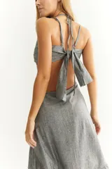 Vestido midi gris con textura de lino, breteles finos, escote con jareta ajustable, cut-out en la cintura y falda asimétrica con volantes.