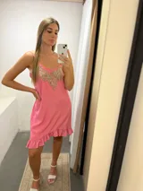 Vestido corto rosado con breteles finos, escote en V con aplique bordado dorado y volados en el ruedo.