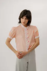 Blusa de manga corta abullonada color salmón con rayas blancas, cuello mao, detalles florales en contraste en la botonera y los puños, y cierre frontal con botones.