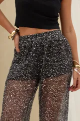 Pantalón largo negro con lentejuelas y acabado brillante, de corte recto y tejido semitransparente.