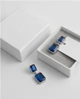 Caravanas colgantes de acero con diseño de doble rectángulo y piedras azules engarzadas.