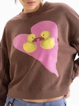 Buzo marrón de cuello redondo, mangas largas y calce amplio con efecto lavado desgastado. Presenta un diseño estampado en el frente con un corazón rosado y dos patitos.