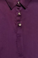 Camisa de cuello solapa y manga larga acabada en puño ancho, confeccionada en tejido satinado de color violeta. Cuenta con cierre frontal mediante botones dorados.