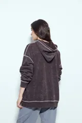 Buzo canguro de calce relajado, color marrón con efecto lavado y costuras a la vista en contraste. Cuenta con capucha integrada y bolsillo frontal tipo canguro.