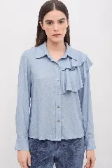 Camisa de manga larga color celeste, con cuello clásico y detalle de volado asimétrico en el frente. Cierre frontal con botones.