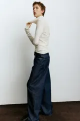 Jean de tiro alto con corte baggy, confeccionado en denim de algodón. Presenta diseño de cinco bolsillos, cierre frontal con botón y silueta de pierna curva con volumen en la cadera.