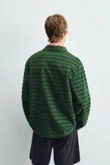 Polo de manga larga con cuello solapa y cierre frontal de botones. Presenta un tejido jacquard texturizado con rayas horizontales en tonos de verde.