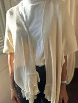 Ruana color crema de tejido de punto calado, con mangas cortas y volados en el borde inferior.