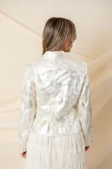 Chaqueta plateada de cuero ecológico laminado, con cuello solapa, cierre cruzado con broche y detalles de cierres y tachas.