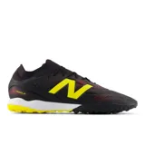Championes de fútbol New Balance modelo Tekela V5, diseñados para césped artificial. Presentan un empeine de microfibra en color negro con detalles en rojo y el logo 'N' en amarillo, cuello tejido para mayor ajuste y suela de goma con entresuela de EVA para mayor comodidad.