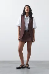 Short pollera de tiro medio con silueta recta y diseño tipo falda en el frente, confeccionado en tela de sastrería color marrón.