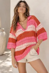 Remerón de punto tejido con diseño de rayas horizontales en tonos rosado, naranja y beige, con cuello polo y mangas cortas holgadas.