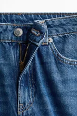 Jean de tiro alto y corte acampanado, confeccionado en denim de algodón. Presenta diseño de cinco bolsillos, cierre frontal con botón y costuras decorativas laterales.