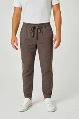 Pantalón tipo babucha de corte ajustado, confeccionado en tejido de algodón color gris topo. Presenta cintura elástica con cordón ajustable, bolsillos laterales y puños elásticos en los tobillos.