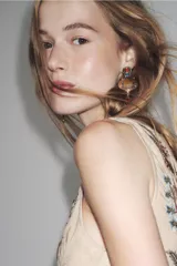 Pendientes colgantes de estilo étnico o bohemio, con base metálica dorada envejecida. Presentan un diseño escalonado con varias piedras incrustadas: una piedra central ovalada color ámbar/mostaza, rodeada de pequeñas piedras blancas, y rematados con una piedra colgante en forma de gota color caramelo. Incluyen detalles en piedras pequeñas de color turquesa y rosado en la parte superior.