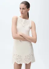 Vestido corto de tejido de punto fino color crema, con cuello barco y sin mangas. Presenta un diseño recto con detalles calados en forma de flores en el pecho y en el ruedo, el cual tiene un acabado festoneado.
