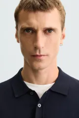 Polo de punto negro, manga corta, con cuello solapa y cierre frontal de tres botones. Presenta un calce regular y acabados en rib en mangas y ruedo.