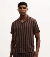 Camisa de manga corta con cuello solapa y cierre frontal de botones. Presenta un diseño de rayas verticales con textura jacquard en tonos marrones.