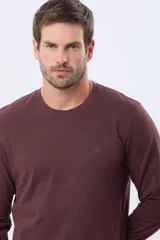 Remera de manga larga con cuello redondo, confeccionada en tejido de algodón con textura jaspeada. Presenta un pequeño logo bordado en el pecho y una etiqueta decorativa en el puño.