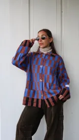 Saco abotonado de tejido de punto con diseño de cuadros en tonos azul y marrón. Presenta corte recto oversize, cuello camisero, cierre frontal con botones en forma de corazón y dos bolsillos delanteros.