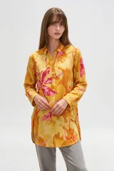 Camisa de lino larga y holgada, de color amarillo con estampado abstracto en tonos fucsia y naranja, con cuello camisero, cierre frontal parcial con botones y aberturas laterales en el dobladillo.