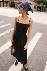 Vestido midi negro de escote recto con tirantes finos ajustables, espalda descubierta y falda amplia con bajo de bordados perforados a tono y detalle de puntilla.