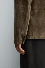 Sobrecamisa de corte regular confeccionada en piel con acabado serraje. Presenta cuello solapa, cierre frontal con botones y bolsillos de plastrón en el pecho y la parte inferior.