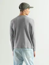 Remera de manga larga con cuello redondo, confeccionada en tejido de algodón tipo mini piqué. Presenta un diseño versátil con puños elásticos en las mangas, ideal para usar como prenda base o como buzo ligero.