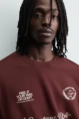 Camiseta de manga corta y cuello redondo, color granate oscuro, con estampado frontal en blanco que incluye texto y un escudo circular.