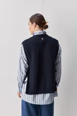 Chaleco tejido de punto color beige, con cuello redondo, terminaciones en rib y lazos laterales regulables que permiten ajustar la prenda.