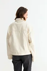 Campera de jean color crudo con diseño de corte holgado, cuello clásico, cierre frontal y detalles de desgastes en toda la prenda.