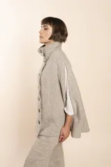 Capa color beige con textura de espiga, cuello alto con botones y aberturas laterales para los brazos. Confeccionada en lana fina sin teñir.