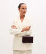 Cartera bandolera pequeña marca Satinato, confeccionada en poliuretano color bordó. Presenta una estructura rectangular con solapa frontal, cierre magnético y correa larga de cadena metálica dorada.