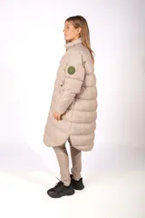 Campera puffer larga de color negro con acabado brillante, cierre frontal con botones a presión y cuello alto. Presenta un parche circular en la manga izquierda.