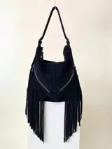 Bolso tipo hobo color tostado, hecho de cuero con flecos largos en el frente y dos bolsillos con cierre. Tiene una manija regulable con hebillas metálicas.