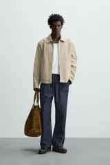 Cazadora color beige de algodón, corte recto, con cuello solapa, cierre frontal con cremallera, manga larga con puños abotonados y bolsillos laterales de ojal.