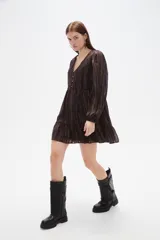 Vestido corto de manga larga con cuello en V y cierre frontal de botones. Presenta un diseño holgado con falda de volado en el ruedo y un estampado sutil de rayas verticales brillantes sobre fondo oscuro.