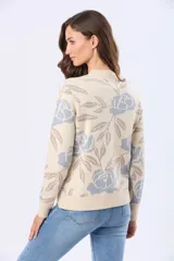Buzo tejido en jacquard con estampado floral en tonos azul y marrón sobre base color crema. Presenta cuello redondo y puños acanalados.