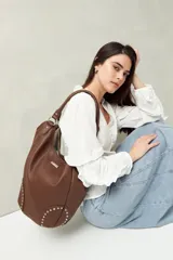 Bolso shopper marrón de símil cuero texturizado con asas cortas y detalles de tachas metálicas.