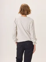 Remera de manga larga color negro con cuello en V y puños fruncidos. Presenta un estampado sutil en tonos grises y blancos en el centro del pecho, simulando un ramillete de flores secas.